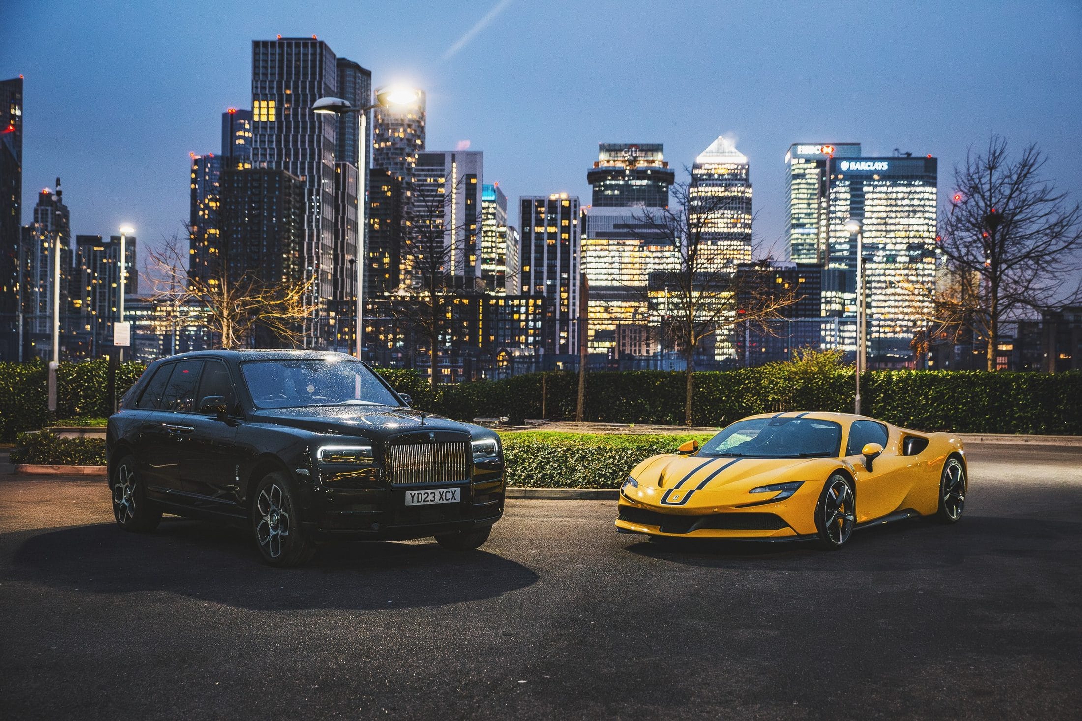 A Rolls-Royce Cullinan and a Ferrari SF90 against the Canary Wharf skyline at night